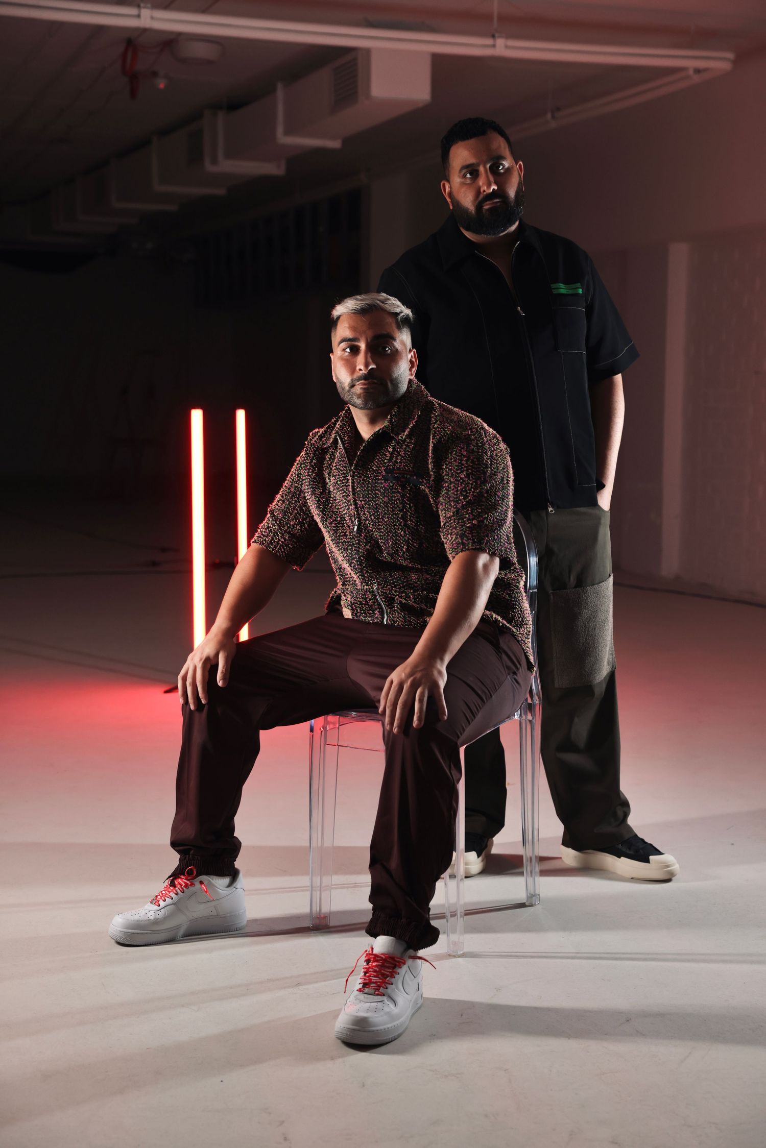 Person sitting on chair in dramatic red lighting wearing casual attire and sneakers.