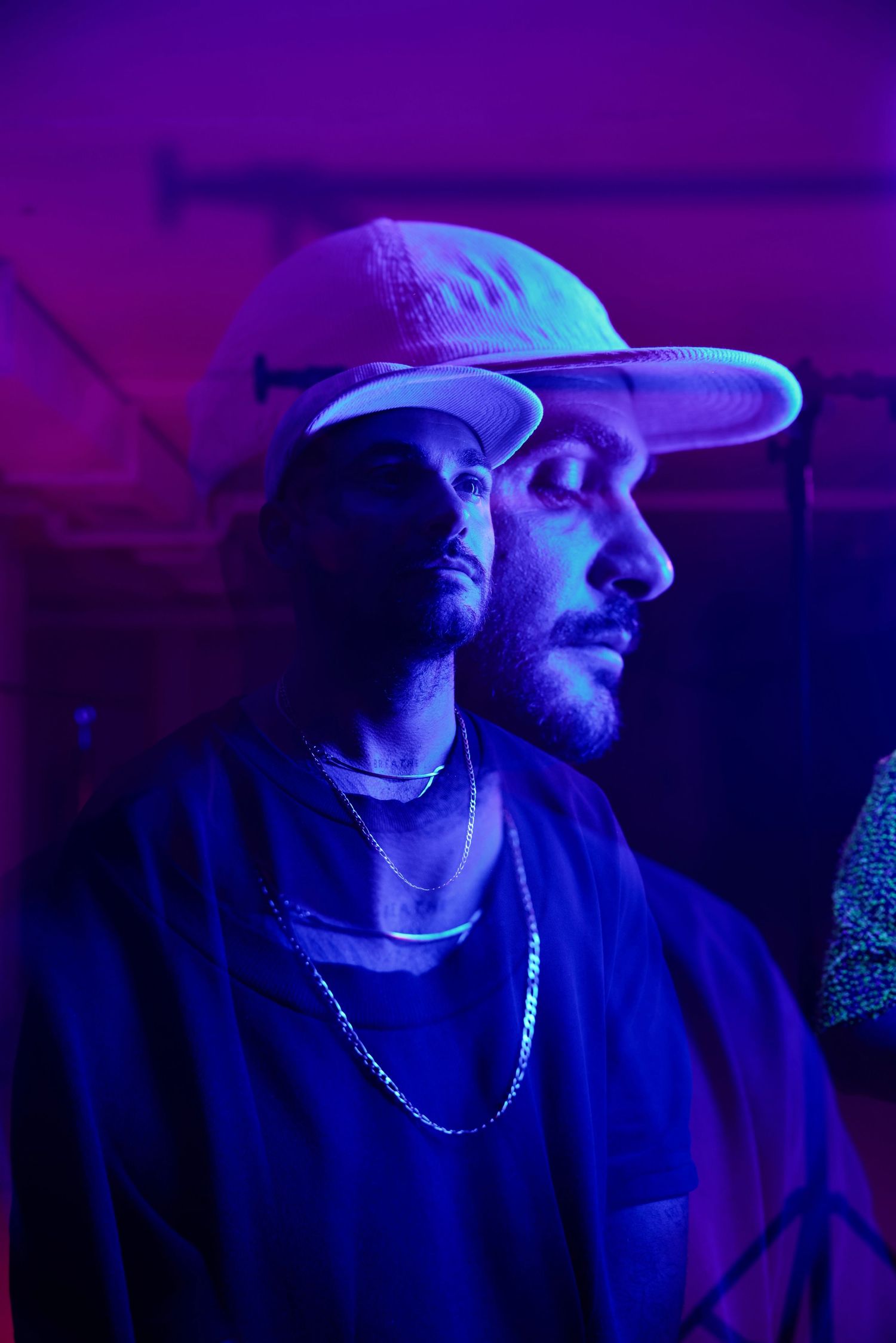 Profile shot of person in baseball cap under dramatic purple and blue lighting.