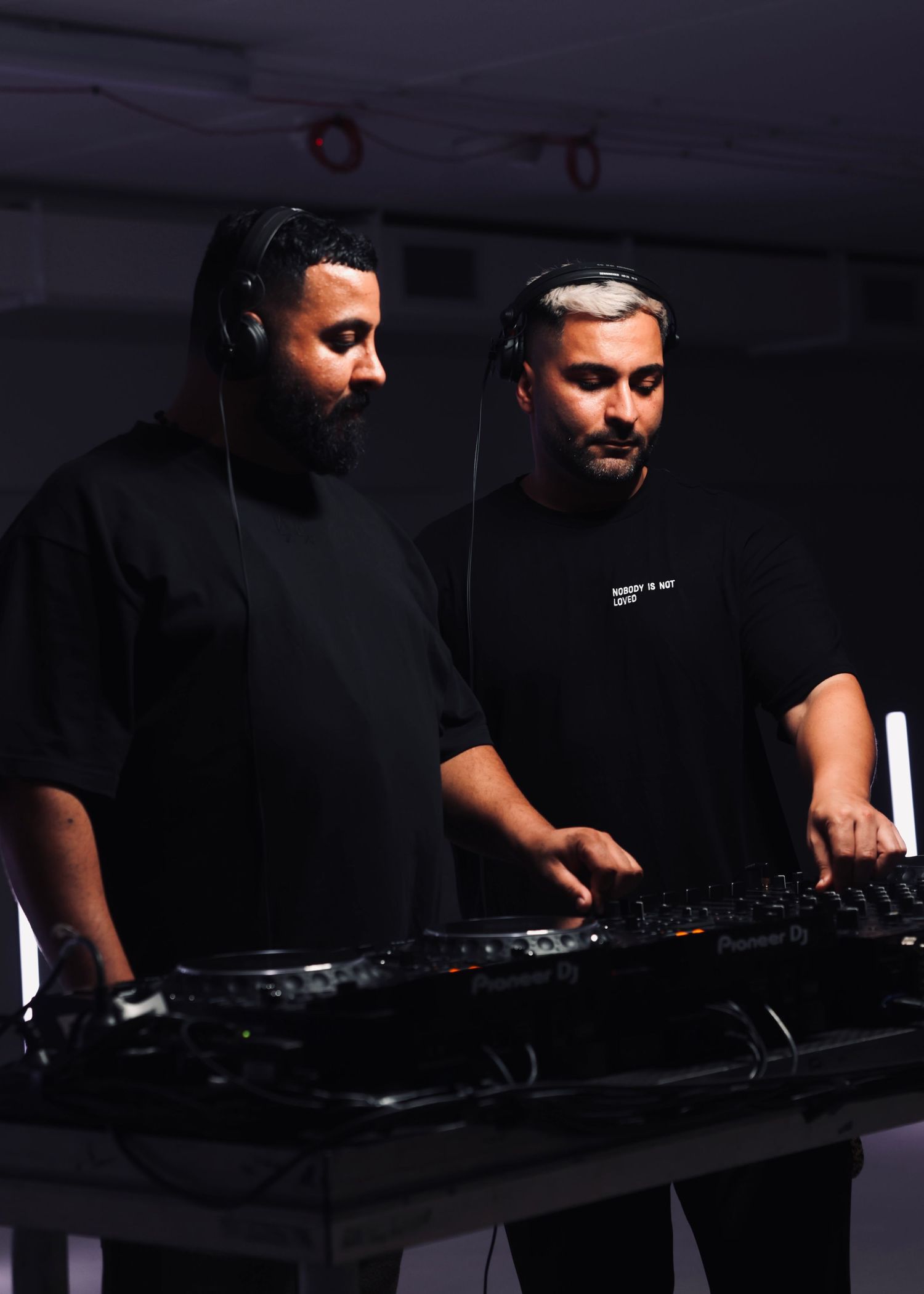 DJs performing at mixing console in dark room with dramatic lighting.