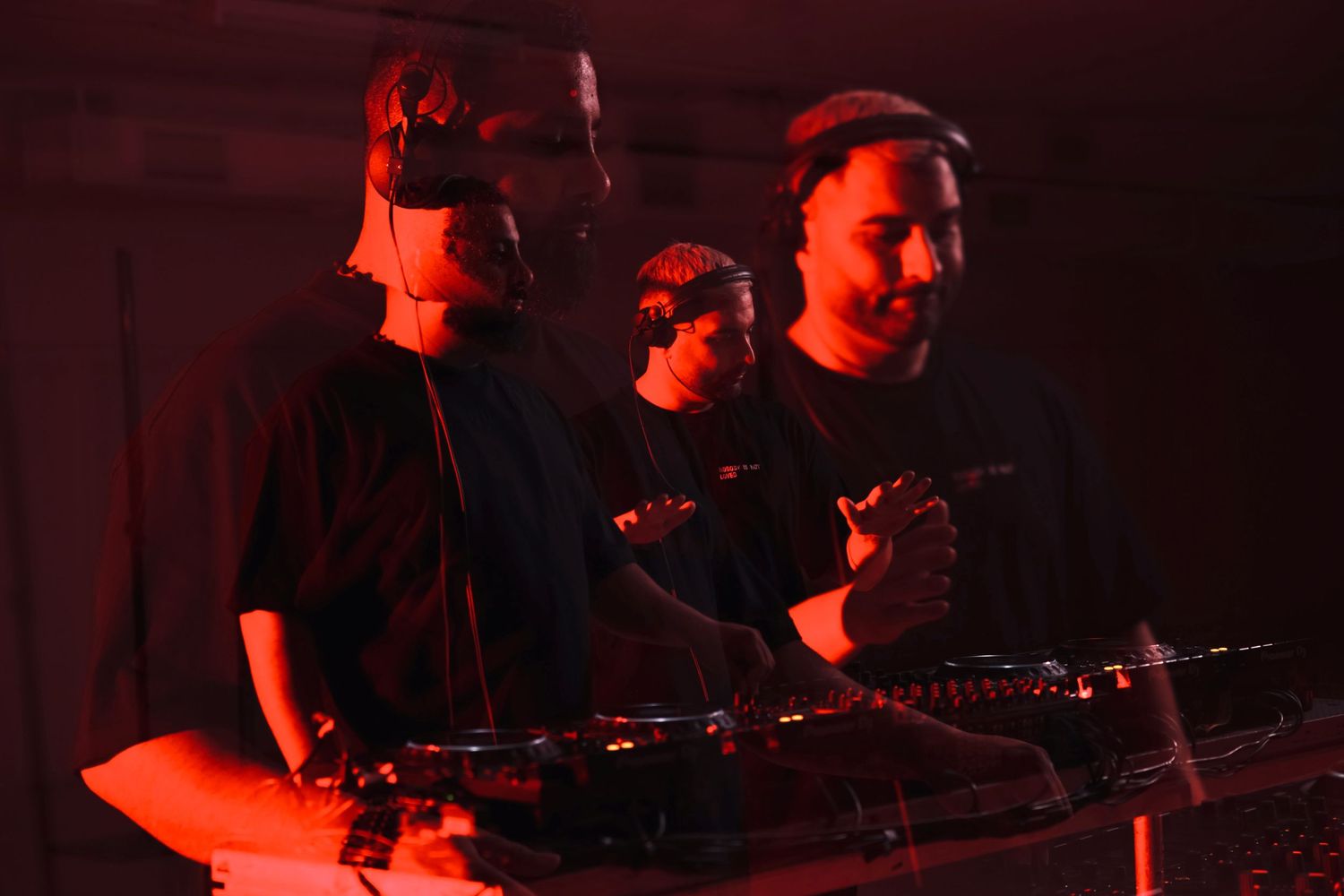 Musicians performing on stage bathed in red lighting with electronic instruments and controllers.