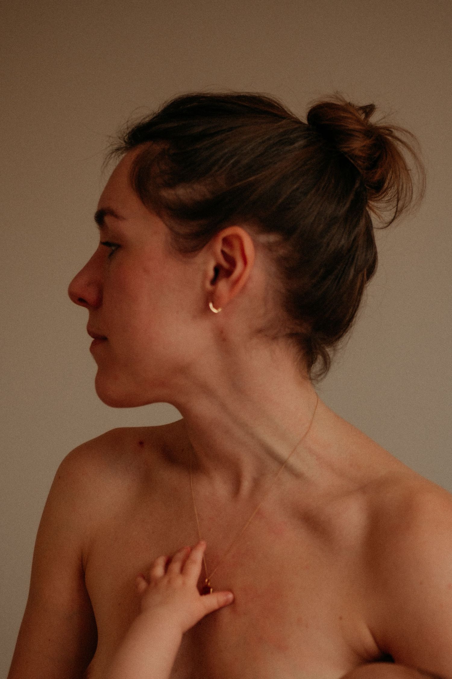A woman with her neck turned and her small babies hand reaching up to her necklace during a breastfeeding session in Gateshead