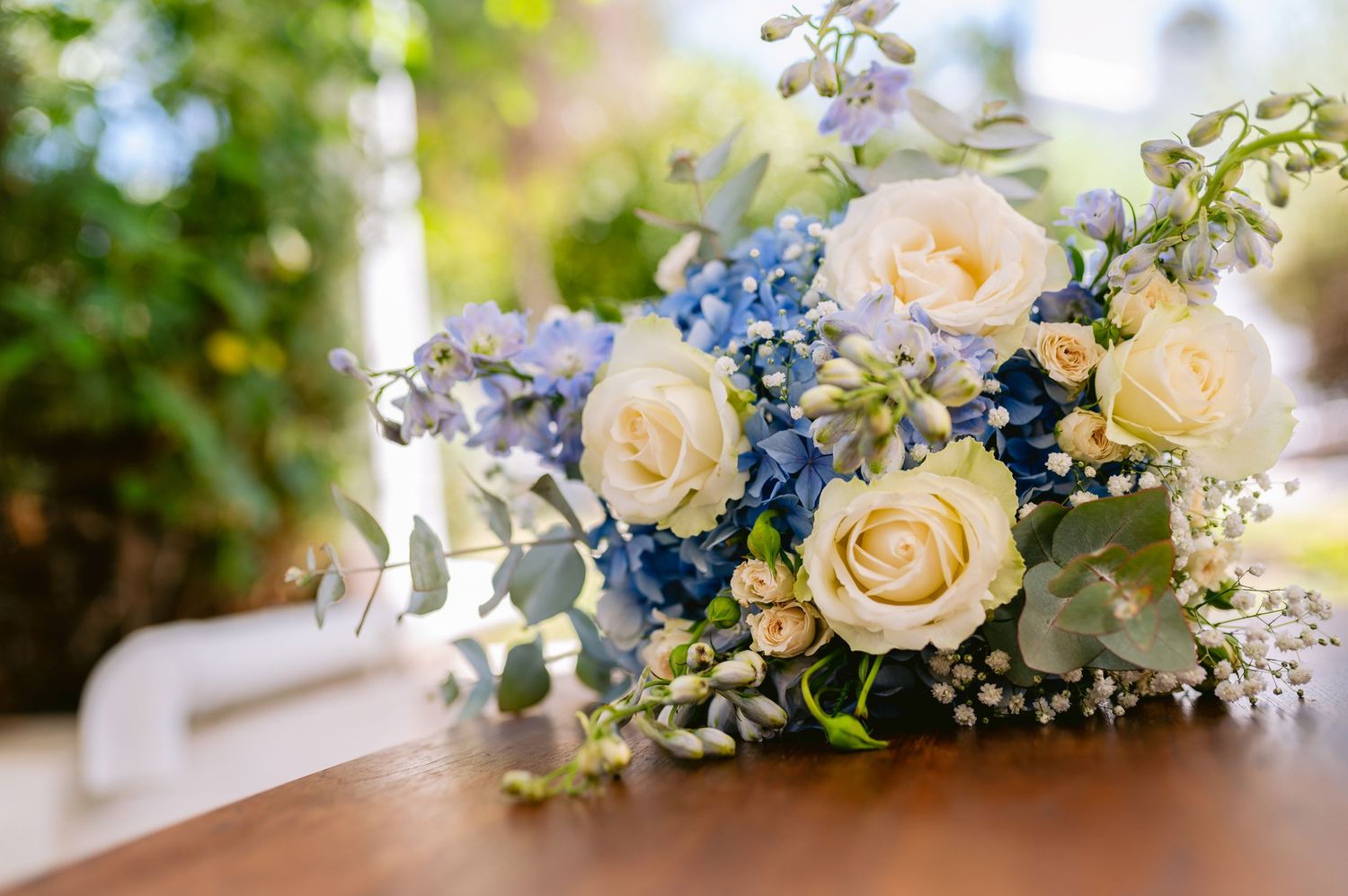 Delicate floral wedding arrangements featuring cream roses and blue delphinium flowers with baby's breath accents.