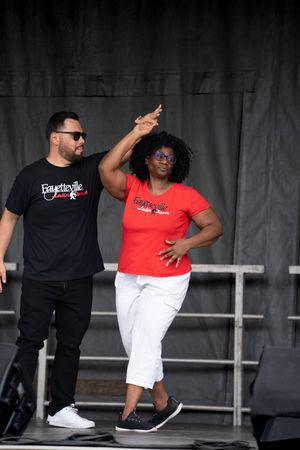 Dancers in red and black outfits perform choreographed moves on an outdoor stage.