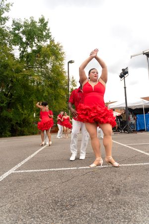 Dancers in red costumes performing a choreographed routine in a parking lot.
