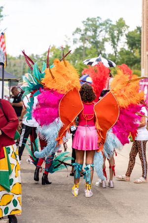 Dancers in bright feathered costumes with orange, pink, and turquoise plumes performing at an outdoor festival.
