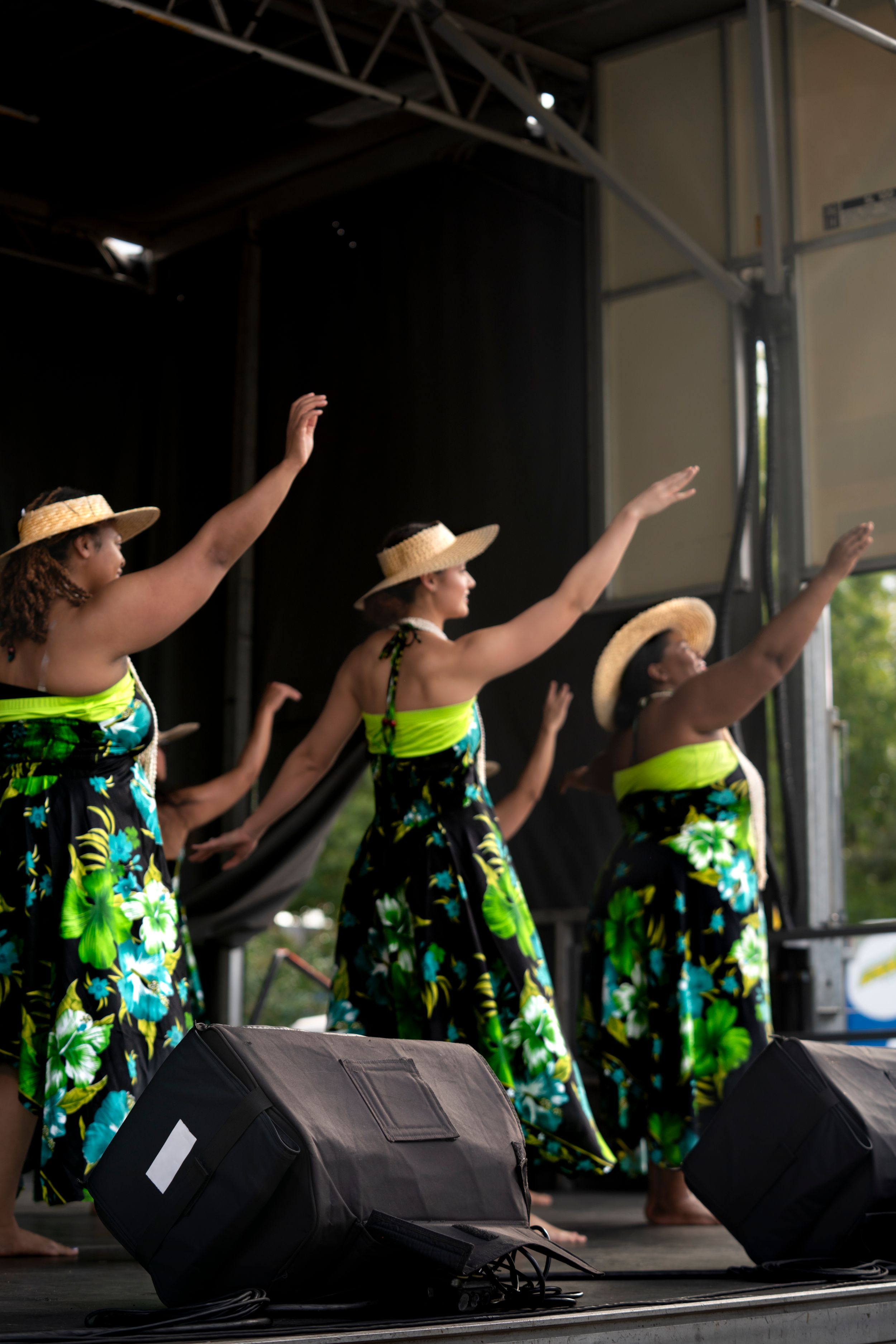 Dancers in tropical print dresses and straw hats perform synchronized movements on stage.