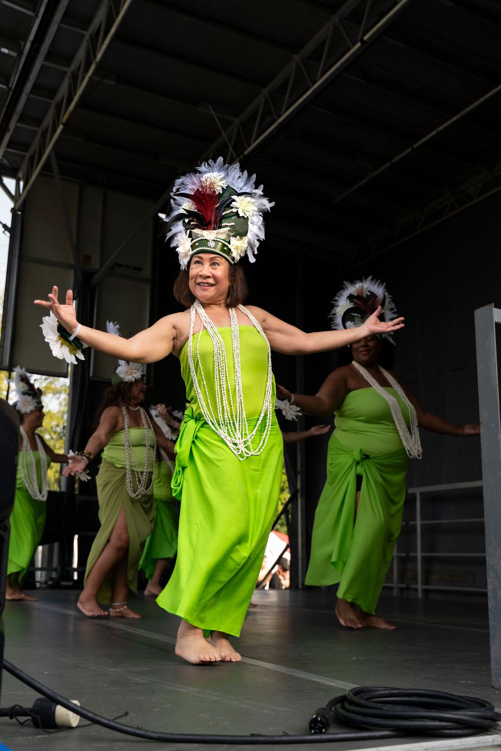 Polynesian dancers in bright neon green dresses perform traditional movements during a cultural dance show.