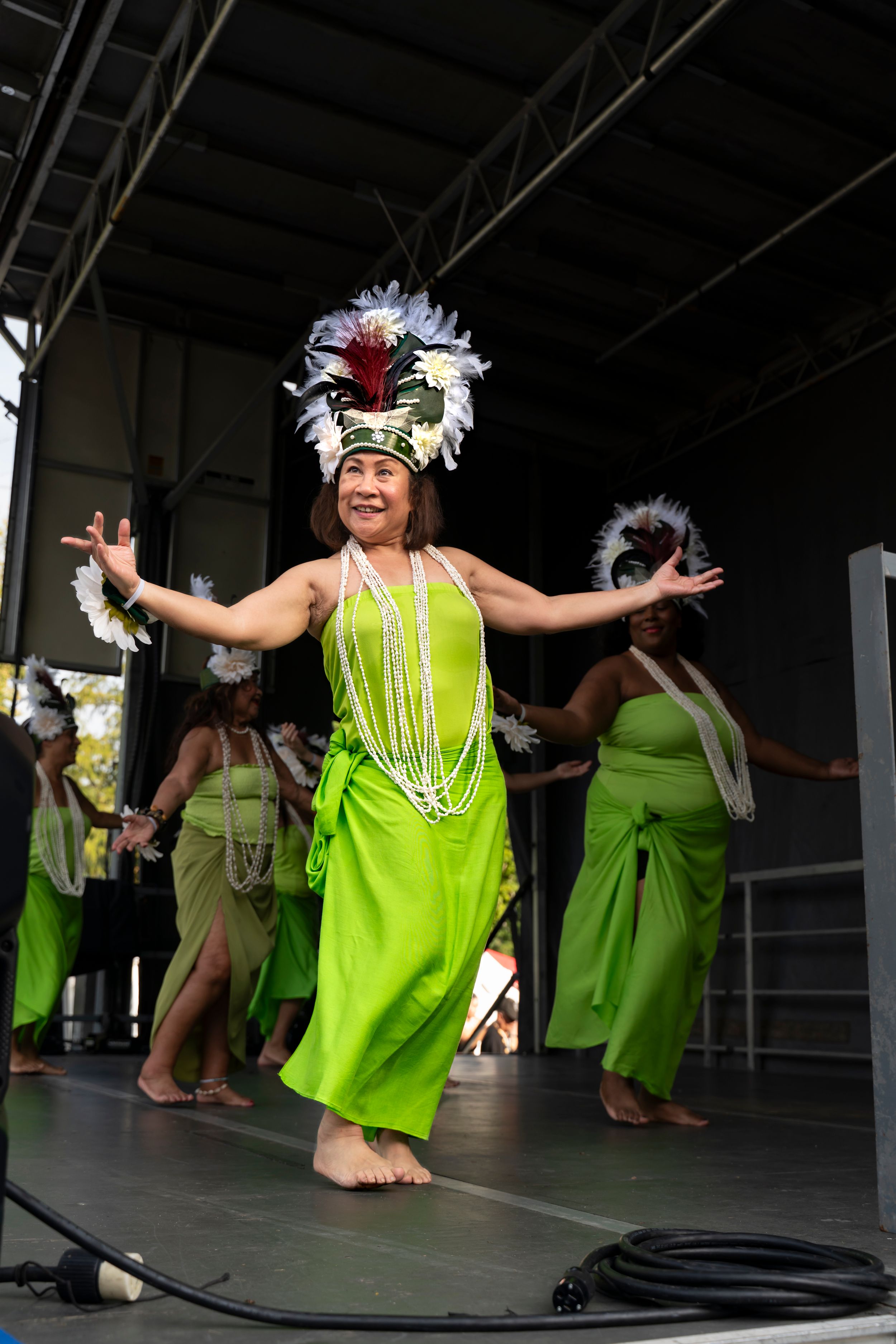 Polynesian dancers in bright neon green dresses perform traditional movements during a cultural dance show.
