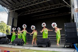 Dancers in bright green grass skirts perform traditional Hawaiian moves on an outdoor festival stage.