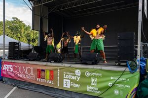 Performers in bright costumes dance energetically on outdoor festival stage.