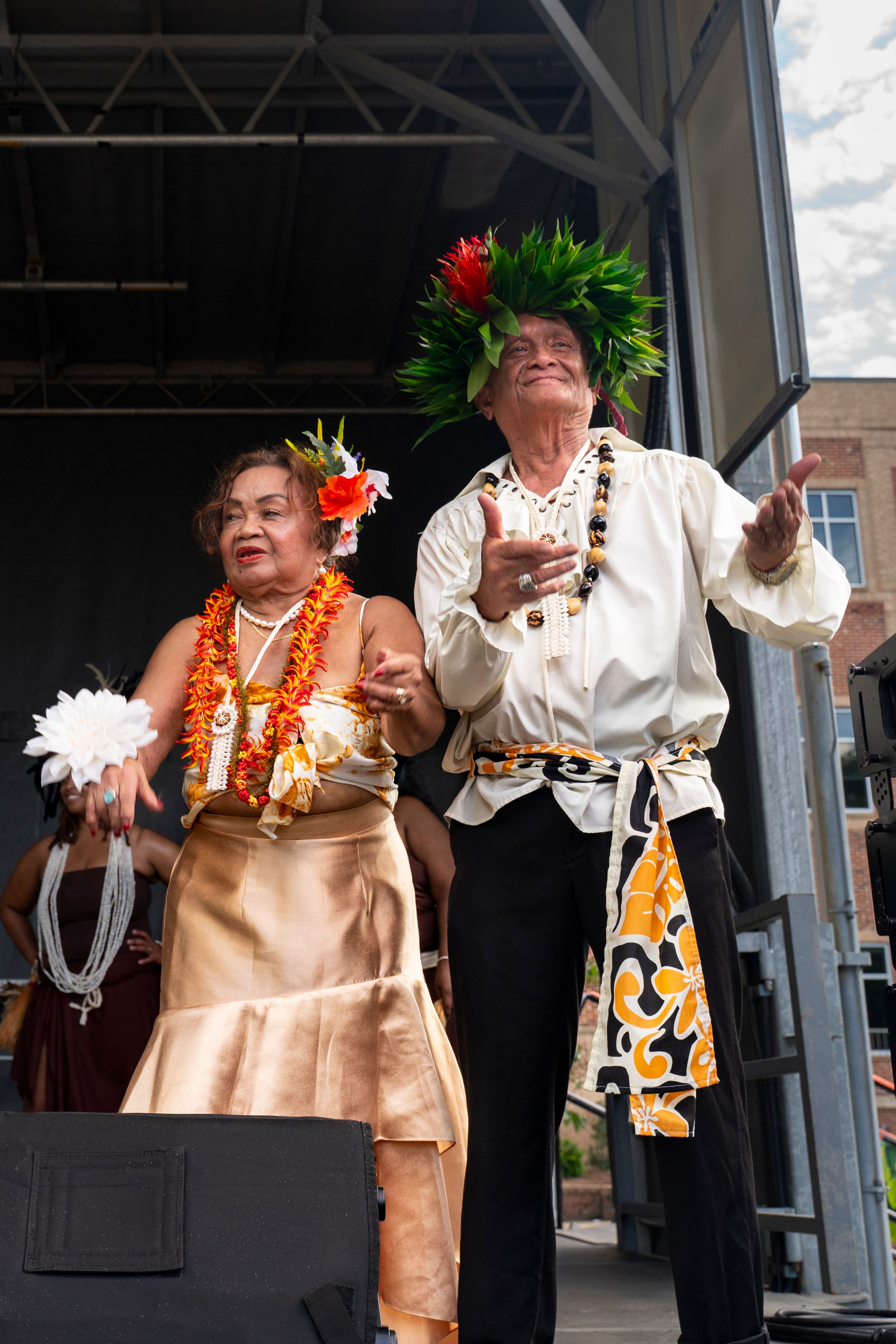 Dancers in traditional Hawaiian attire with leis and floral headpieces perform on stage.