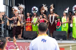 Performers in vibrant traditional Pacific Islander costumes singing on stage at a cultural festival performance.