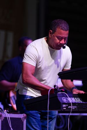 Musician in white t-shirt performs on Yamaha keyboard during live concert performance.