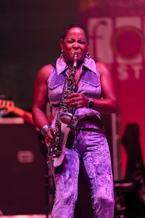 Saxophonist performs passionately in purple attire under dramatic stage lighting.