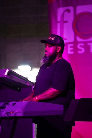 Musician plays keyboard under purple stage lighting at a festival performance.