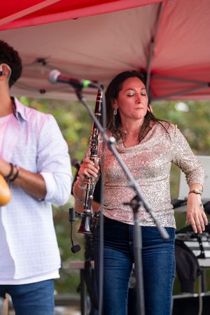 Musicians perform under a red tent canopy at an outdoor event with a person playing a clarinet.