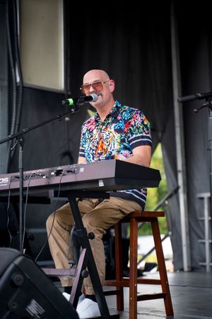Keyboard player in a colorful shirt performing on stage with electronic equipment.