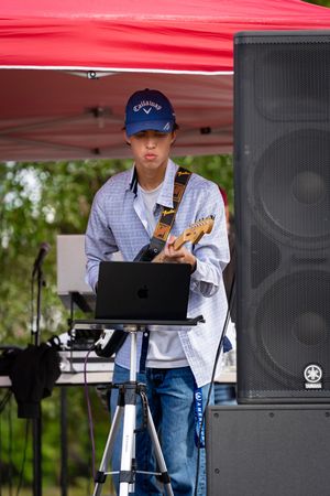 Musicians perform under a red tent with laptops and audio equipment set up on stands.