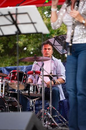 Drummer performs on stage with a full drum kit during an outdoor concert performance.