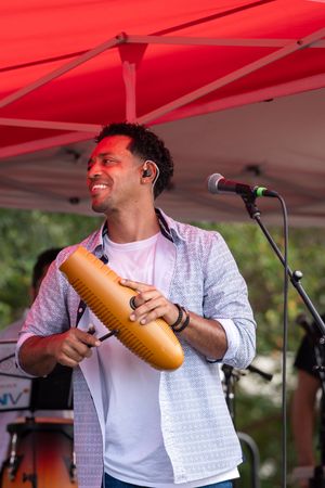 Performer plays a wooden percussion instrument under a red canopy during a festival performance.