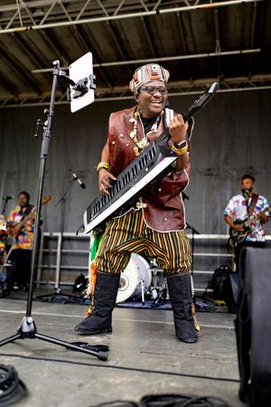 Musicians perform on stage with keyboard players in coordinated outfits at a festival.