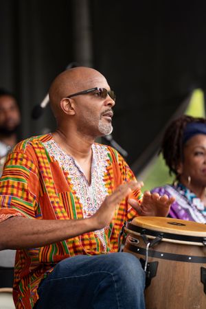 Percussionist in colorful African print shirt plays drums during outdoor festival performance.