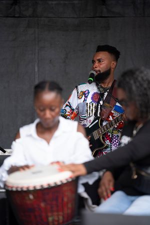 Musicians performing on stage with colorful patterned clothing and instruments against a dark background.