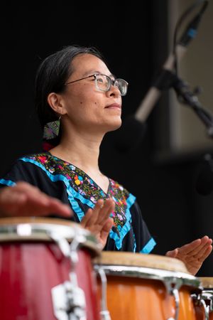 Musician in traditional dress plays percussion instruments during cultural performance.