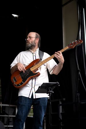Bass guitarist in white shirt performing on dark stage with instrument.