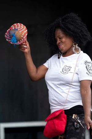 A performer in a white t-shirt holds up a decorated tambourine with festive red and blue details at an outdoor event.