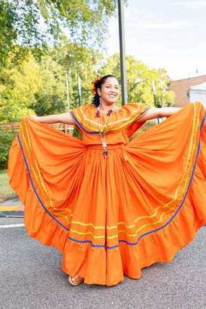 Dancer in bright orange traditional Mexican dress twirls to display the full flowing skirt.