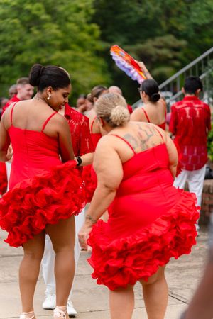 Dancers in bright red tutus and white pants perform a synchronized line dance routine outdoors.