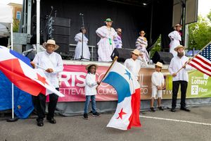 Cultural festival performers holding flags and banners line up outside a community venue.