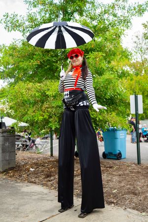 Person in striped top and black dress holding parasol poses in garden setting.