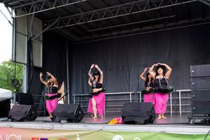 Performers in bright pink outfits dancing on an outdoor stage during a festival performance.