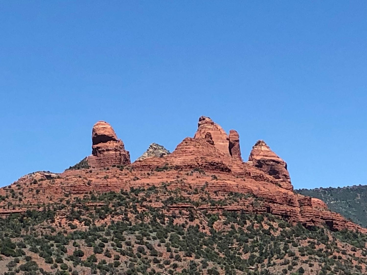 Red sandstone rock formations rise against clear blue sky in Sedona, Arizona's desert landscape.
