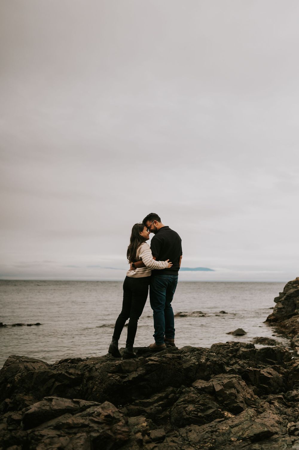Professional Photographer Engagement Photoshoot at Neck Point Park, Nanaimo, Vancouver Island of couple hugging on rocky beach by ocean