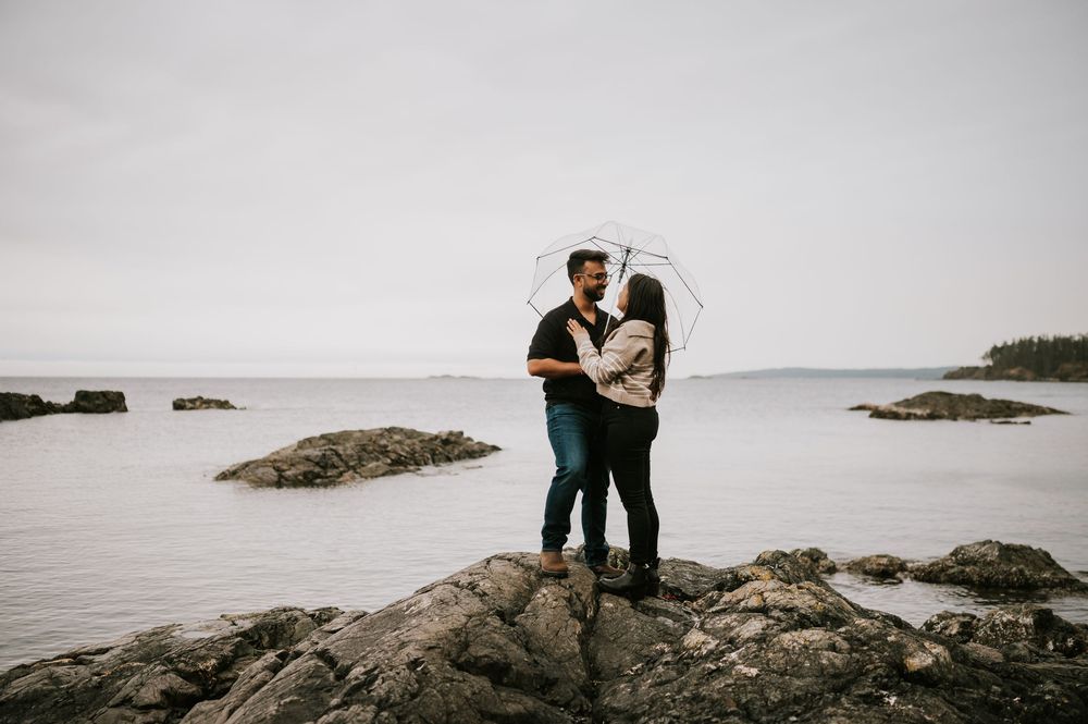 Professional Photographer Engagement Fall Photoshoot at Neck Point Park, Nanaimo, Vancouver Island of couple on rocks in rain with umbrellas