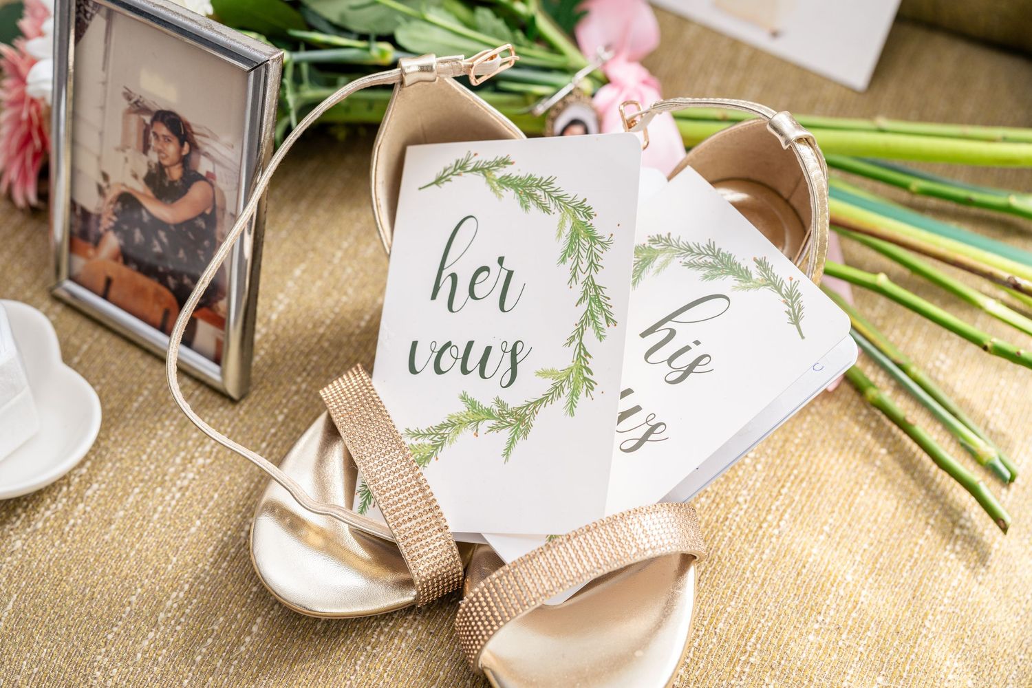 Delicate wedding invitation suite with floral elements, calligraphy and natural greenery stems arranged on beige fabric.
