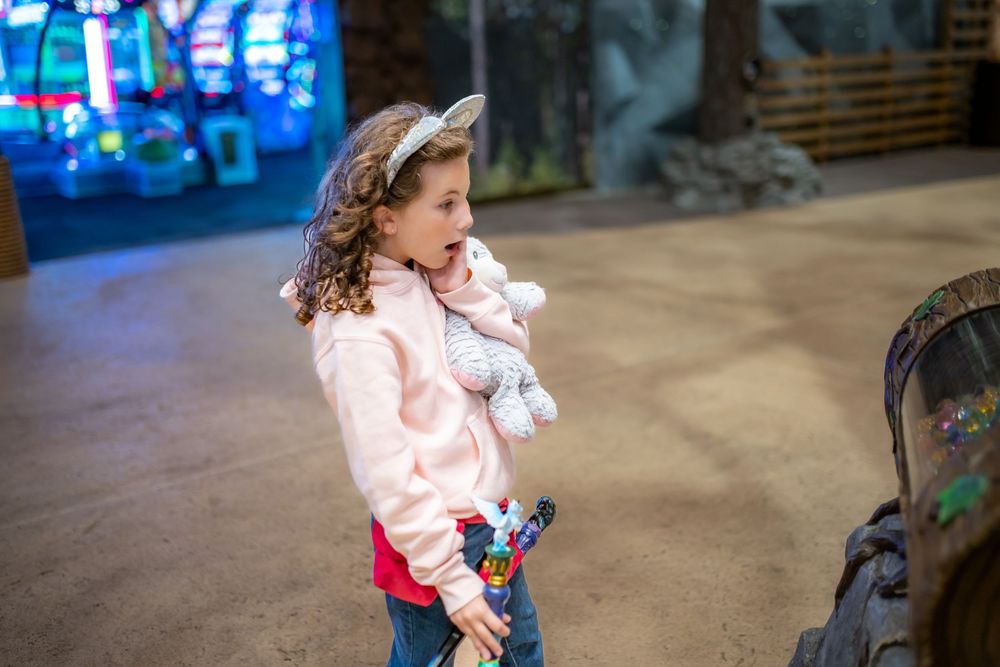 A child in a pink jacket runs and plays with bubbles in an outdoor setting during daytime.