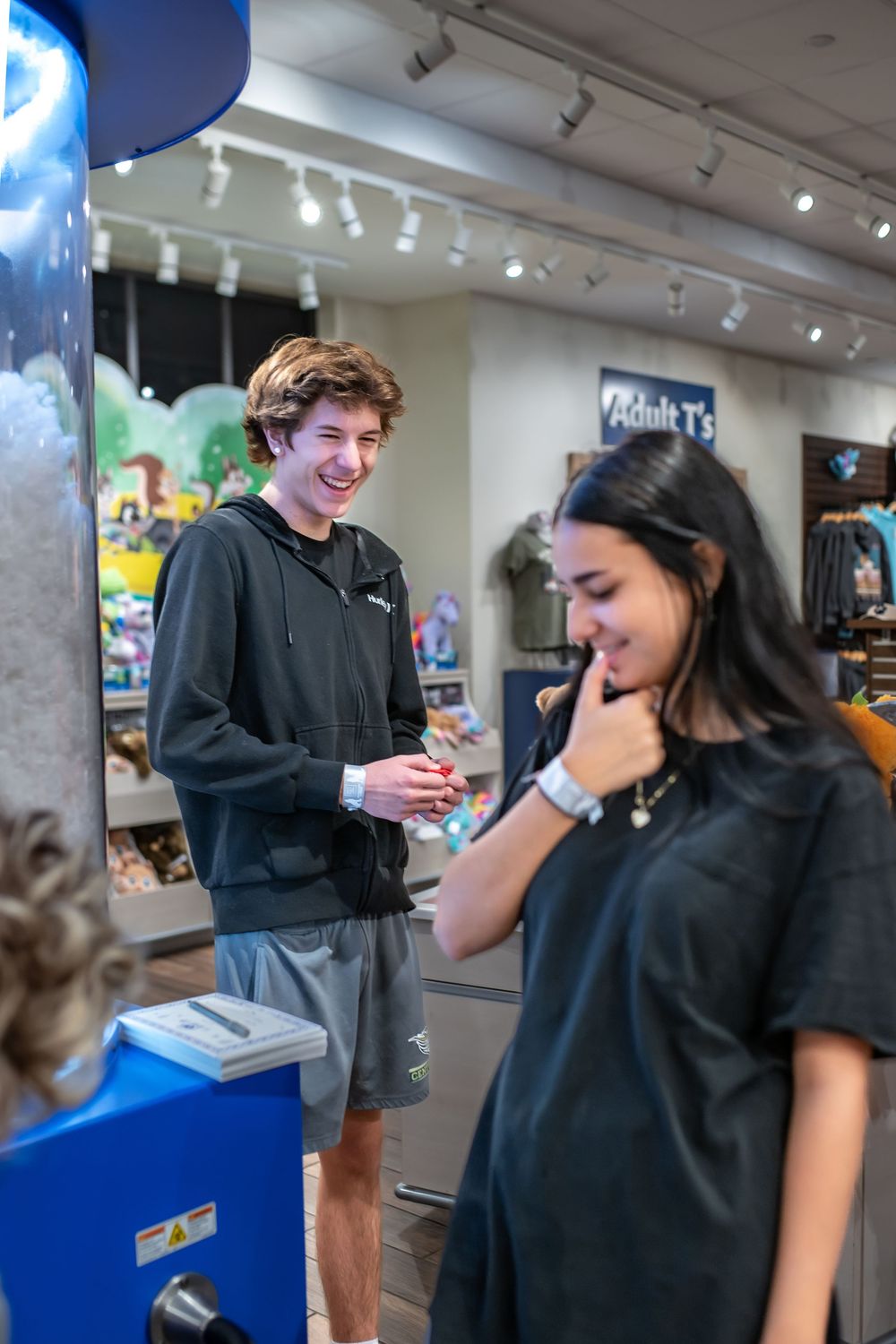 Two people in black clothing share a candid moment of laughter in what appears to be a retail store setting.