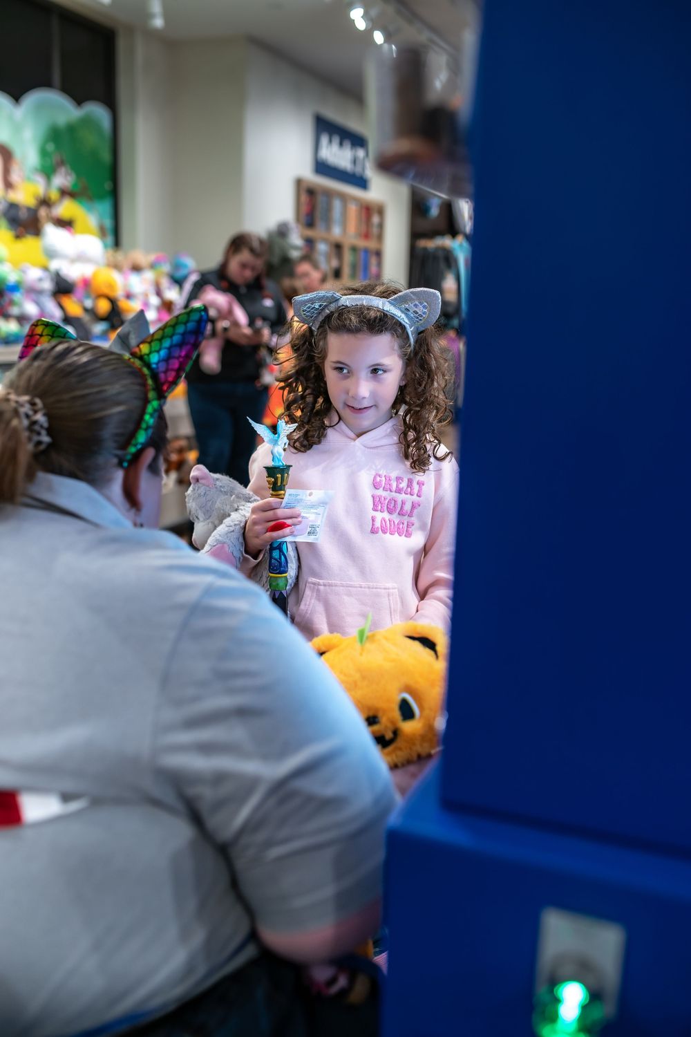 A child in a pink shirt stands among Halloween decorations and plush toys in a retail store.