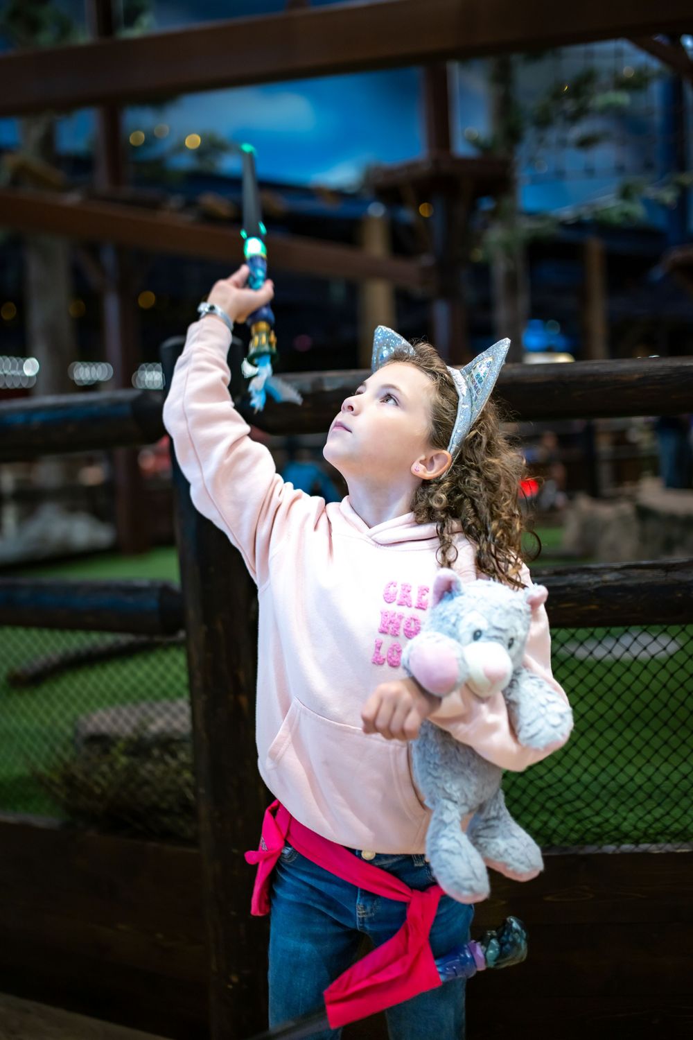 Young child in pink sweatshirt and jeans reaches upward while holding a wand, playing Magic Quest.
