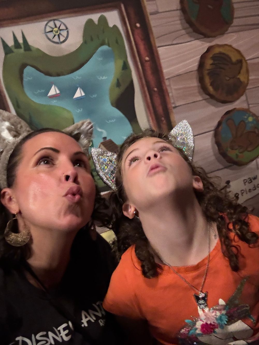 Two people wearing sparkly wolf ears make silly faces while posing together in front of decorative wall art.