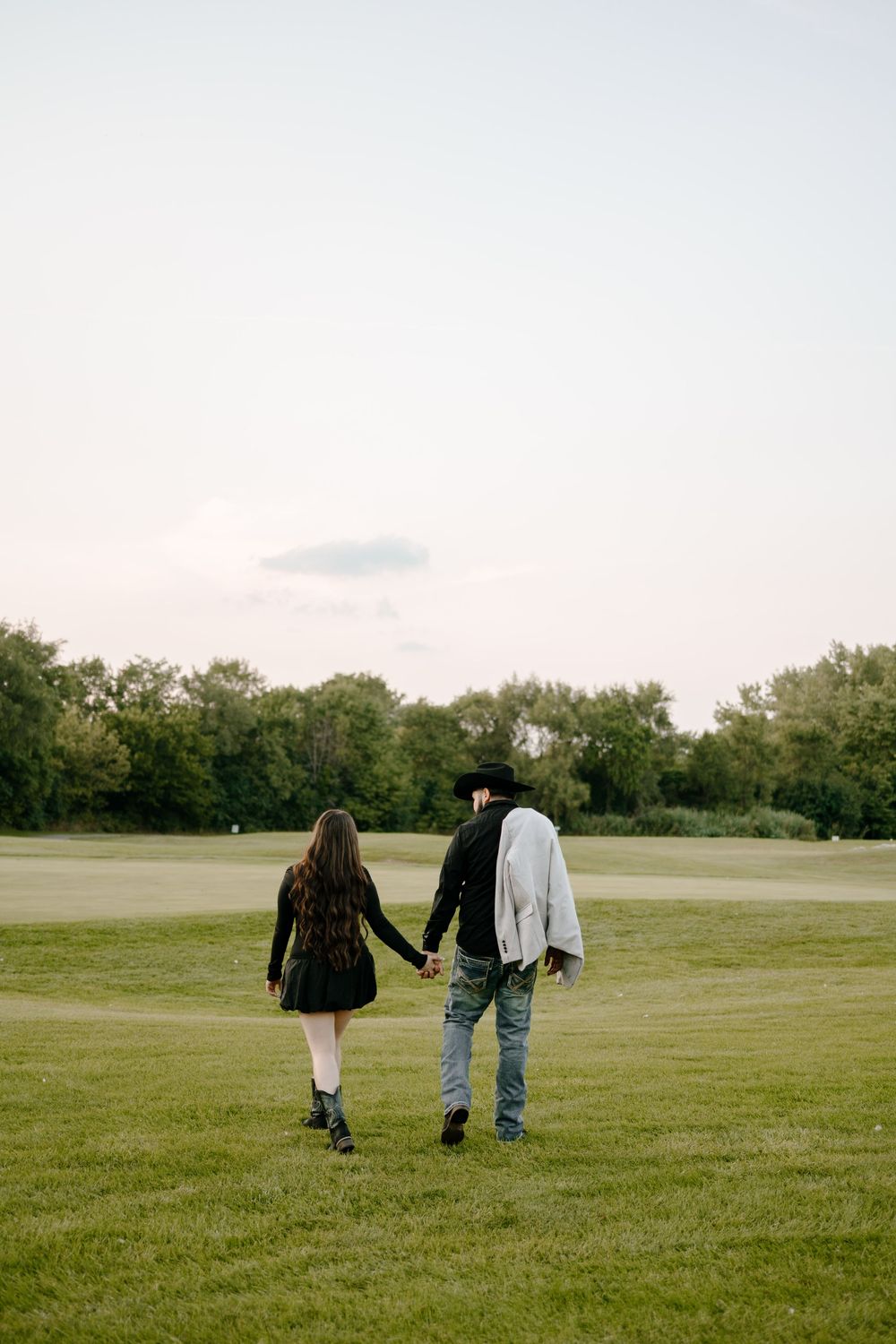 People walking together across a vast green field on an overcast day.