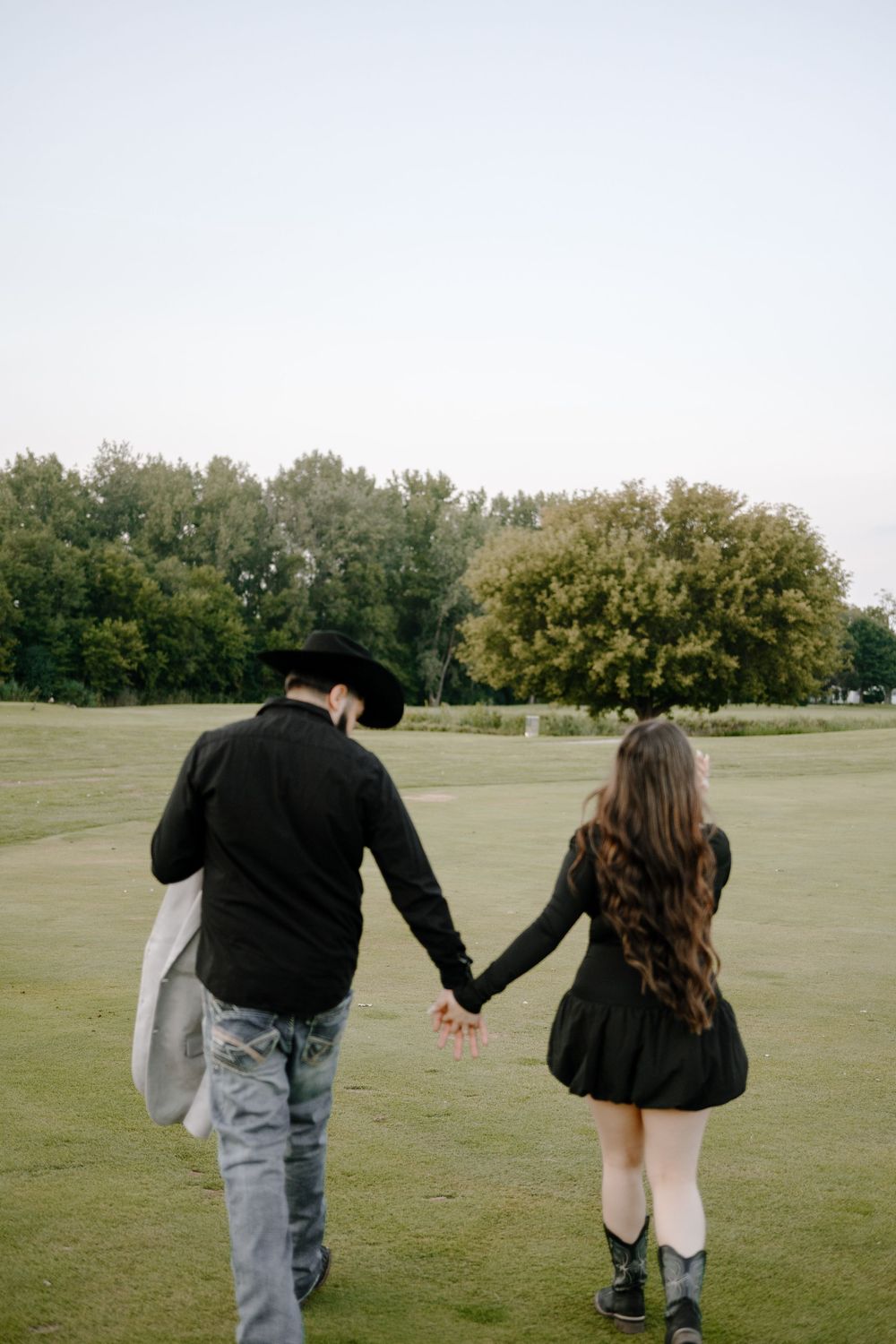 A couple playfully runs and holds hands across a grassy field on an autumn day.