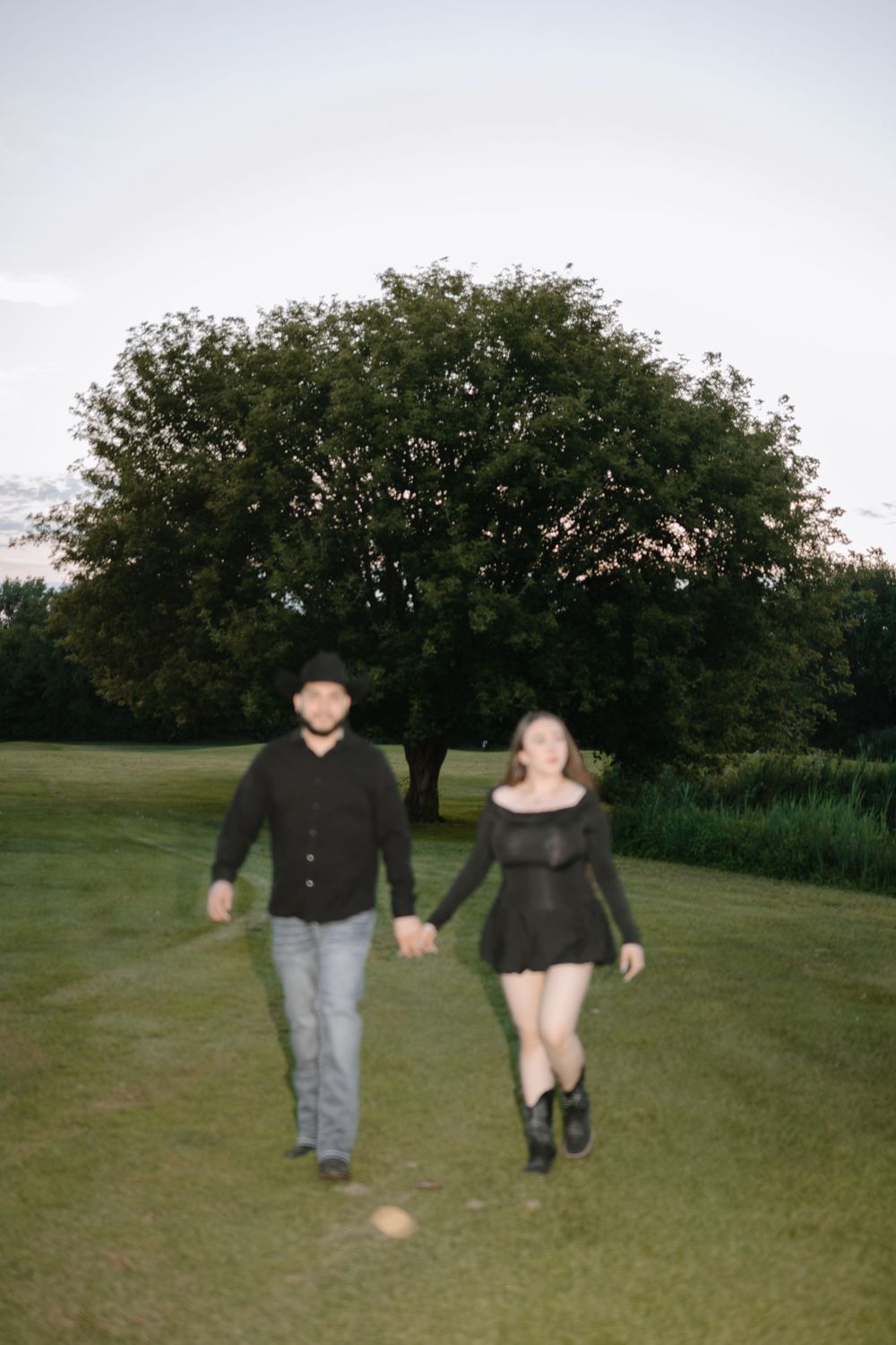 A couple walking together on a grassy field at dusk with trees in the background.