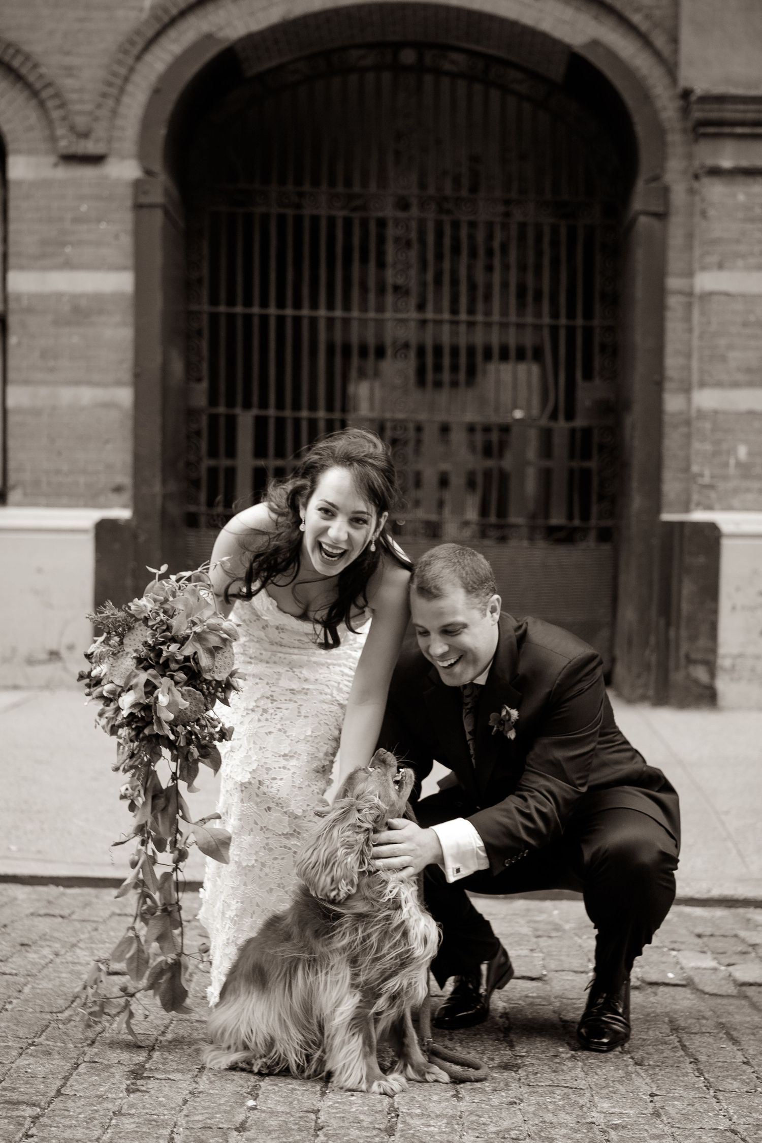 Three black and white photos show a person in formal attire playing with a fluffy dog on cobblestone ground.