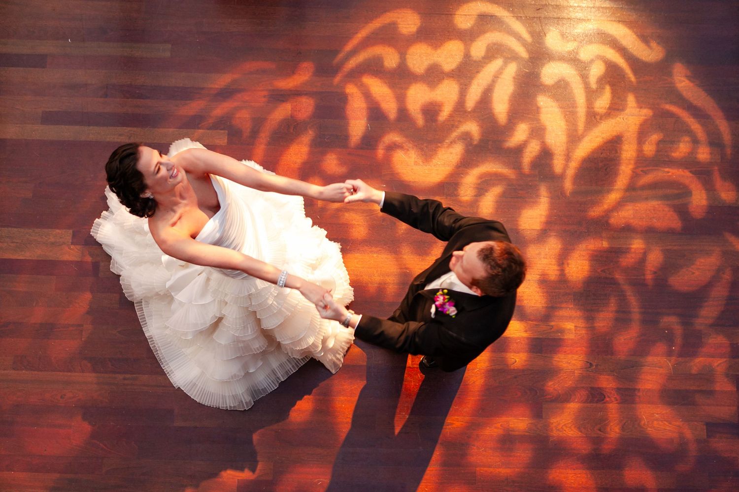Wedding couples performing romantic dance dips on a ballroom floor with decorative orange lighting patterns.