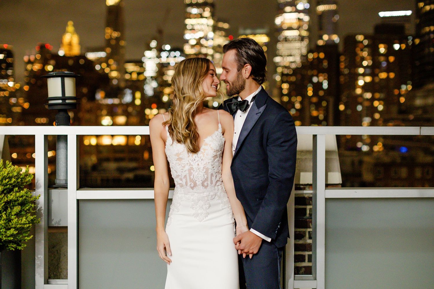 Romantic wedding couple shares intimate moments on a rooftop terrace with city lights in the background.